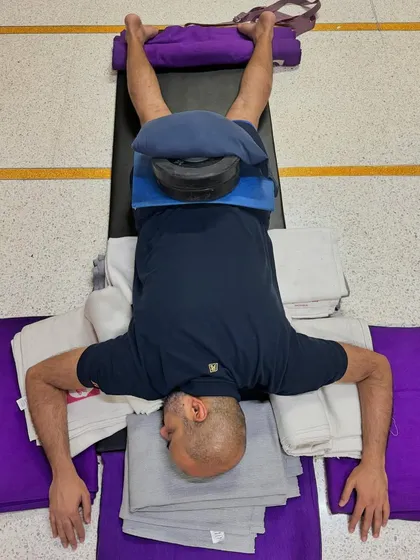 This is an elaborate setup for a deep restorative pose. The extensive use of props, including bolsters and weights, ensures the body is completely supported, facilitating a profound state of relaxation and healing.