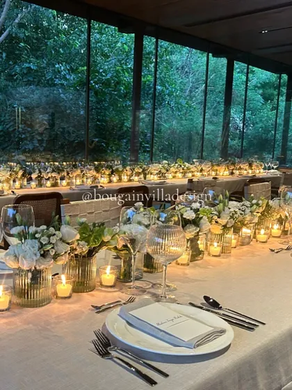 The Central Pavilion at night, with a long dining table aglow with dozens of candles. The floor-to-ceiling windows reflect the intimate scene, while revealing the dark forest outside.