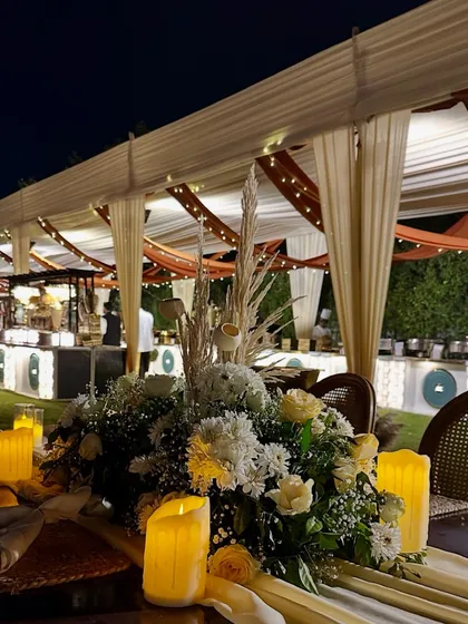 A close-up of a rustic table centerpiece, combining white roses and pampas grass with the warm glow of flameless candles.