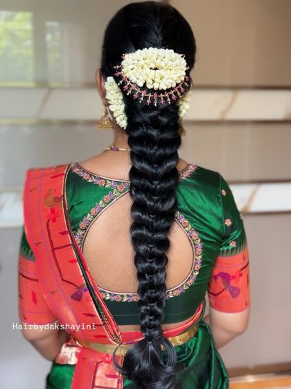 A classic, thick South Indian braid adorned with a traditional jasmine and red flower arrangement, showing a timeless look for a wedding ceremony.