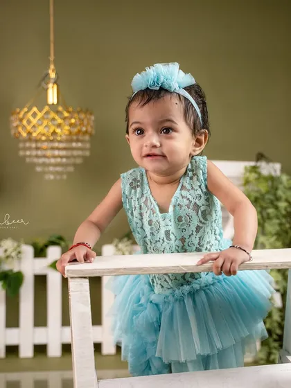 Practicing her standing skills. This one-year-old looks so proud in her lacy teal dress during her milestone birthday shoot.