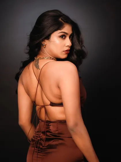 A close-up studio portrait focusing on the model's expression and the details of her backless dress. The lighting is soft yet dramatic, creating an elegant and alluring shot.
