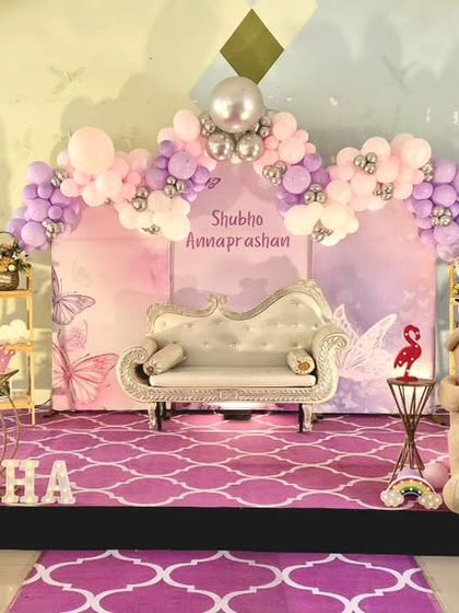 A beautiful butterfly-themed rice ceremony decoration. The setup features a pastel color scheme, a large butterfly wing prop, and a comfortable diwan for the ceremony.