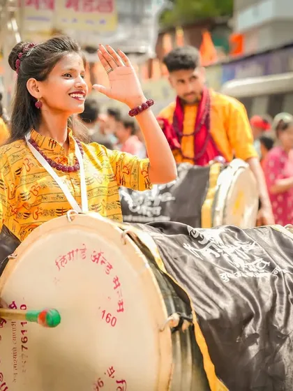 A female dhol player smiles and waves, her energy and joy radiating through the crowd during the procession.