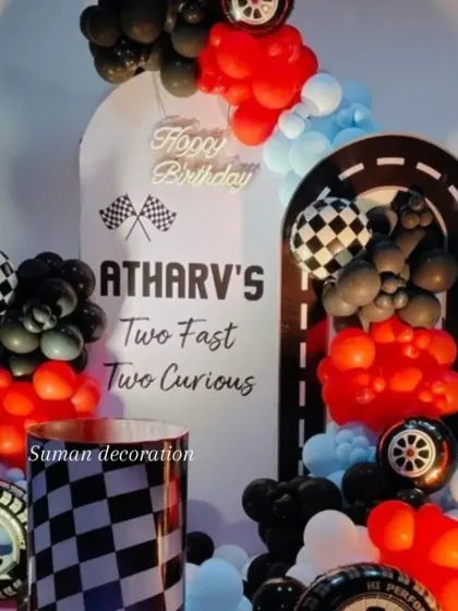 A "Two Fast Two Curious" car racing theme for a second birthday. The decoration includes a checkered flag pattern, tire props, and a balloon garland in red, black, and light blue.