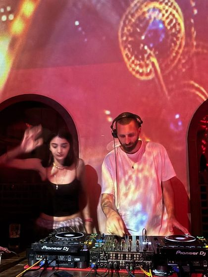 A long exposure shot capturing the motion and energy of a B2B set. It visually represents the flow and dynamic exchange of music between two DJs.