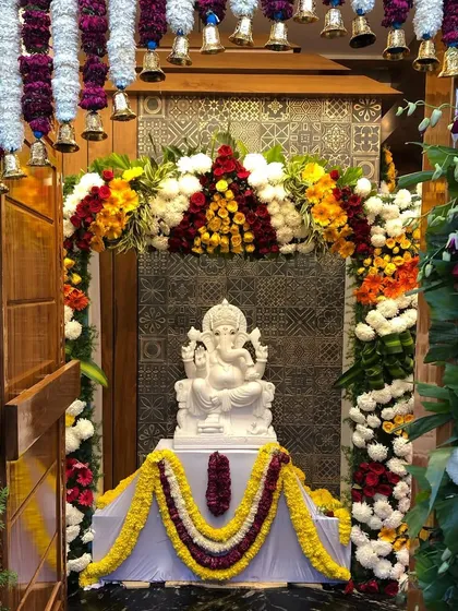 The grand entrance to the pooja room at the "Sanman" residence on the day of the housewarming. The space is adorned with flowers and features a beautiful marble Ganesha idol, creating a welcoming and auspicious atmosphere.