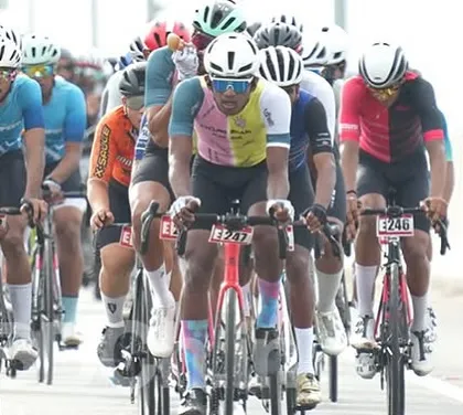 The peloton moves as one organism, with riders from different teams sharing the workload at the front. This is a classic scene from the Bangalore Classic Road Race.
