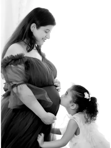 A heartwarming black and white photo capturing a tender moment between a mother-to-be and her daughter, who is kissing the baby bump. We love including siblings to make it a full family celebration.