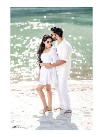 A romantic embrace on the beach, with the sun sparkling on the water behind them. The man gently kisses her forehead, creating a tender and beautiful moment.