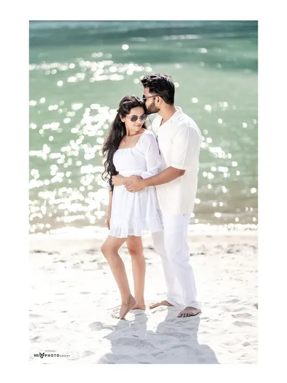 A romantic embrace on the beach, with the sun sparkling on the water behind them. The man gently kisses her forehead, creating a tender and beautiful moment.