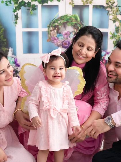A first birthday celebration with the whole family. The little one, dressed as a fairy, is the center of attention, surrounded by her loving family in a beautiful floral setting.