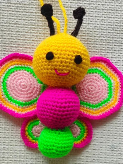 A colorful crochet butterfly with bright pink, green, and yellow wings. This can be used as a toy or a beautiful decoration.