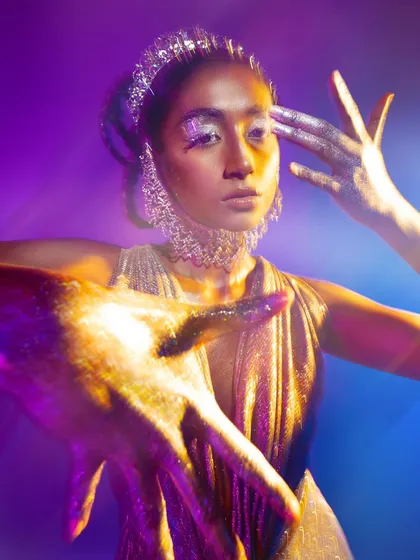 A creative portrait where the model's hands, covered in glitter, become a central part of the composition. The purple and yellow lighting creates a beautiful, high-contrast color palette.