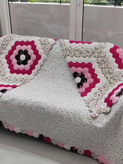 The hexagon flower quilt elegantly draped over a sofa, showing how it can be used as a beautiful throw.