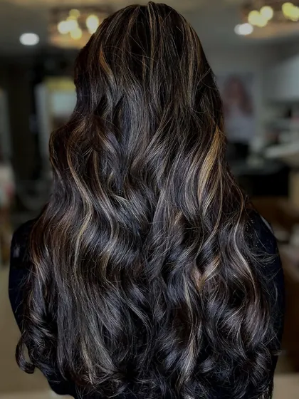 A gorgeous example of subtle balayage on dark, long hair. The highlights are delicately woven in to create a natural, sun-kissed look, styled in beautiful waves.