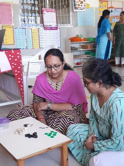 Two educators from Senthil Public School work with the stamp game, a material used for understanding the operations of arithmetic.