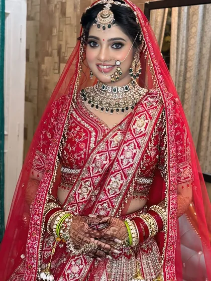 A happy and confident bride smiling for the camera. Her natural-looking base, bright smile, and elegant makeup showcase a modern take on the classic red bridal look.