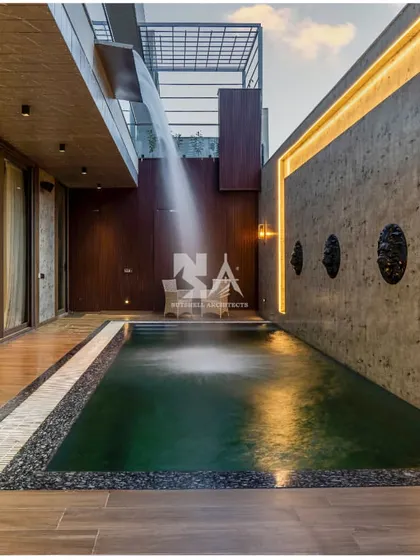 We design spaces that extend living beyond the walls. This tranquil poolside area features a custom water curtain cascading from the balcony above, creating both a visual centerpiece and a soothing auditory experience. The combination of dark water, warm deck lighting, and textured concrete walls makes this a perfect retreat for relaxation or evening entertainment.