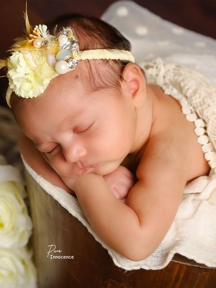 Pure innocence captured in a single frame. This baby sleeps peacefully in a bucket prop, adorned with a delicate headband, showcasing a classic and safe newborn pose.