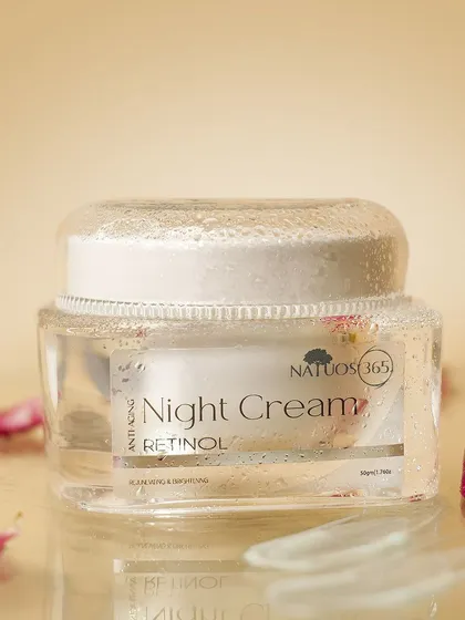 A close-up of Natuos 365 Night Cream with water droplets on the jar, suggesting hydration. The scattered rose petals add a touch of beauty and fragrance.