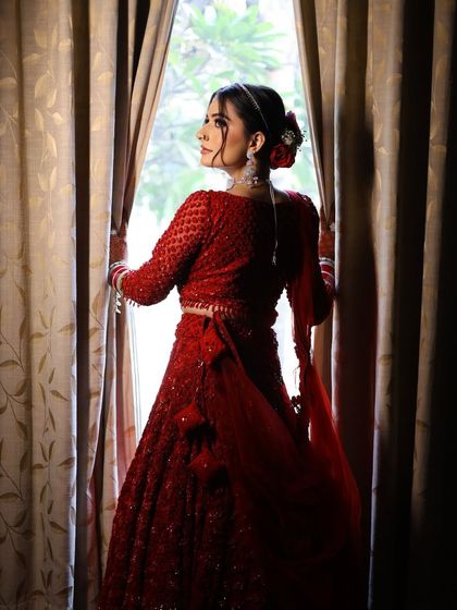 The bride looking out, perhaps waiting for her groom. The natural light beautifully illuminates her features and the intricate details of her red lehenga.