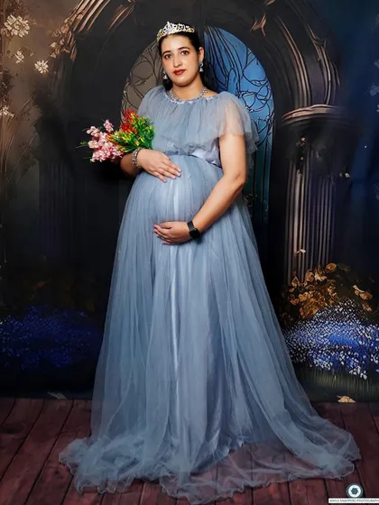 A solo portrait of the mom-to-be from the same session, holding a bouquet and cradling her bump in a beautiful blue gown.