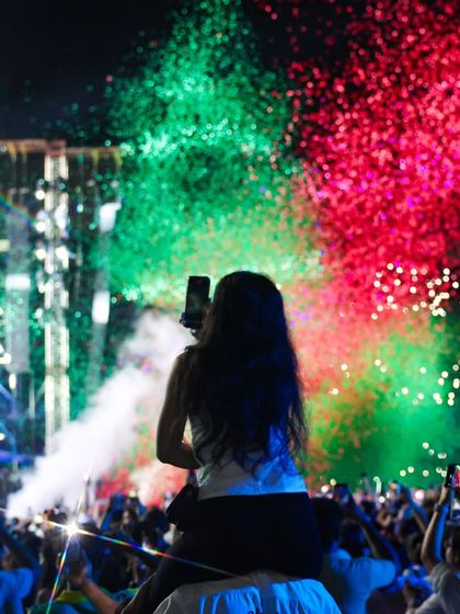 A fan on shoulders captures the perfect shot, framed by a burst of tricolor confetti. This image encapsulates the freedom and celebration we cultivate at our events.