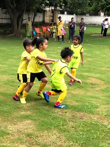 Young players in yellow chasing an orange ball. We believe in steady progress and building confidence step-by-step.