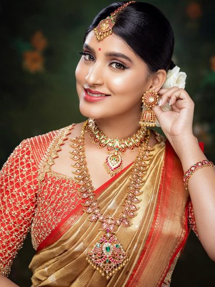 A close-up portrait of Akanksha in her red and gold bridal look, showing her beautiful smile and traditional jewelry.