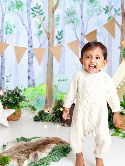 A big, happy roar from our 'Wild One'! This standing shot shows off his adorable cable-knit romper and the charming woodland backdrop.