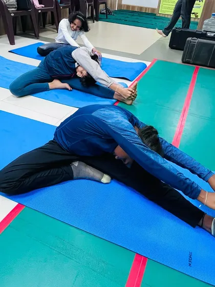 A coach assists students with deep stretching poses. These exercises are essential for maintaining flexibility and preventing muscle strain.