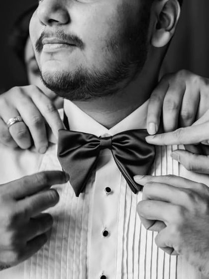 A close-up shot of the groomsmen helping Roshan with his bow tie. It's a moment of friendship and support, capturing the small details that make the day special.