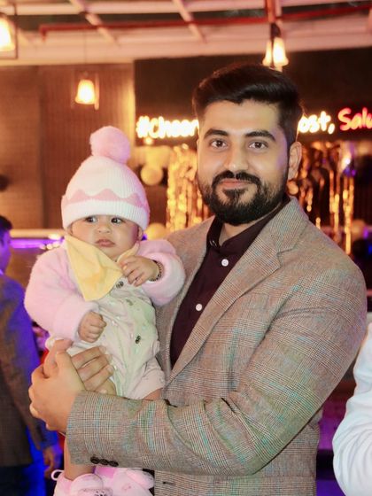 A father holds his baby, who is bundled up in a cute pink hat and outfit.