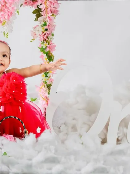 The birthday girl with her arms outstretched, celebrating turning one in a beautiful, heavenly setup.