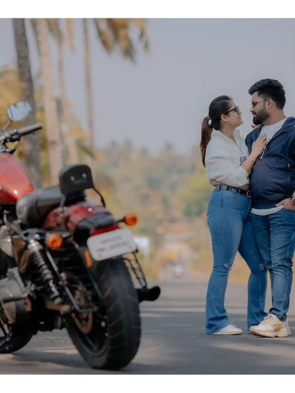 A classic pre-wedding pose with a motorcycle. The couple stands together on a road lined with palm trees, creating a perfect blend of romance and adventure.