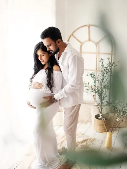 A sweet and gentle moment between the parents-to-be. He stands behind her, wrapping his arms around her and the baby bump in a protective and loving embrace.