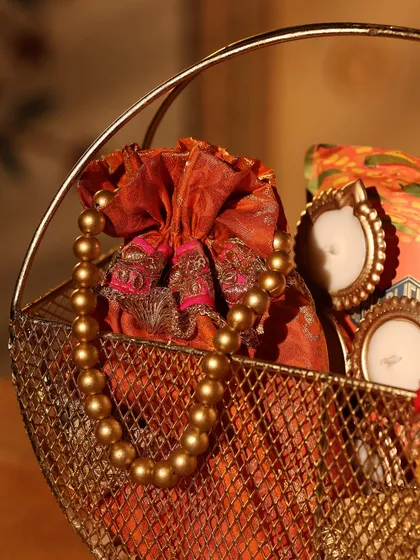It's all in the details. This close-up shows a beautiful Diwali gift basket with an ornate brocade potli, a pearl necklace, and charming miniature photo frames, perfect for adding a personal touch.