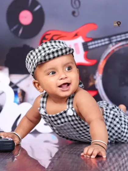 A happy baby crawls across the floor in a music-themed setup, full of energy and joy. The checkered outfit and matching cap complete his rockstar look.
