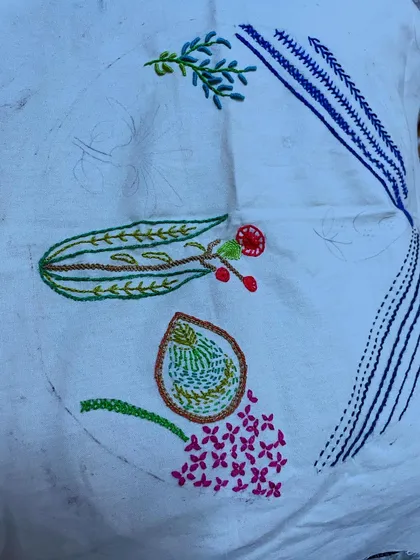Another stage of the floral hoop art project. The combination of different stitches, like the satin stitch for petals and stem stitch for branches, creates a rich and varied texture.