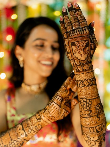A beautiful bride showcasing her full bridal mehendi, with a focus on the detailed work on her left hand.