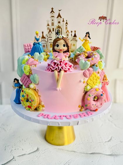 A princess's dream Candyland cake. This pink creation is loaded with sweet treats like edible donuts, chocolate bars, and geometric hearts, and features a custom doll and princess toppers.