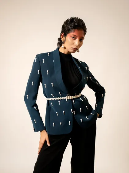 A chic and modern look for a London-based designer. This shot highlights a tailored blazer with unique embellishments, styled with a pearl belt for a touch of elegance.