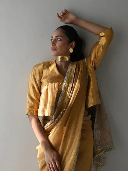 A model glows in a golden chanderi saree. The look is simple, elegant, and timeless, accessorized with a modern gold choker.