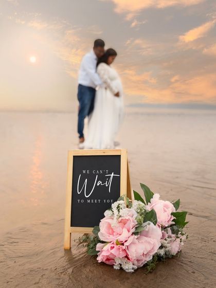 "We can't wait to meet you." A creative announcement shot on the beach, using a chalkboard and flowers to share the couple's excitement.