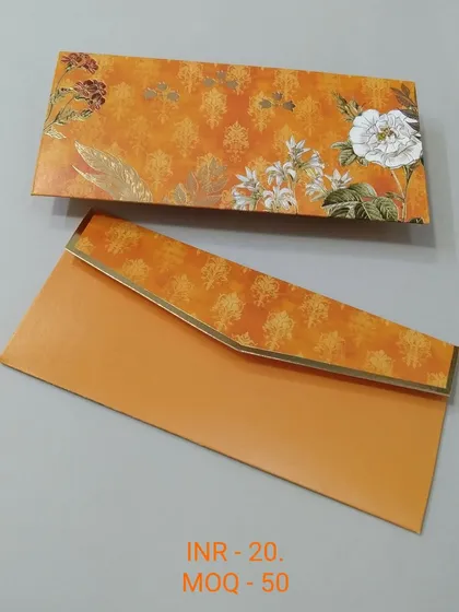 A vibrant orange envelope with a traditional block-print style pattern. The design is complemented by large white and red flowers, making it perfect for festive occasions like Diwali or Haldi ceremonies.