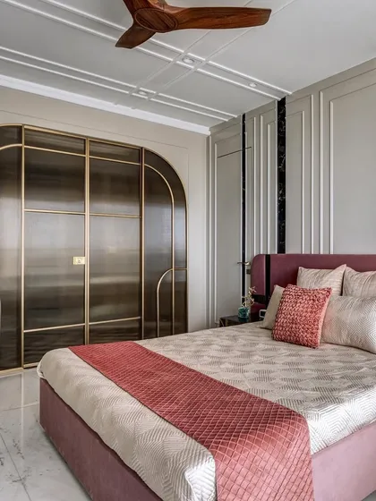This master bedroom is adorned in a soft blush mauve palette for an elegant and romantic feel. The arched, smoked glass wardrobe doors with brass frames are a custom feature that adds a touch of art deco glamour.