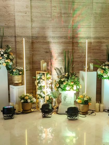 An elegant decor corner featuring floral arrangements on white pedestals, accented with modern tube lighting. This setup adds a touch of contemporary style to the classic white and gold theme.