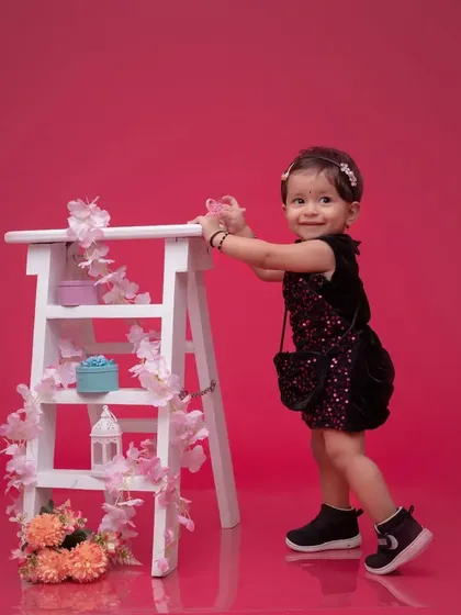 A pre-birthday shoot full of charm. This little girl in a sparkly black dress stands next to a decorative ladder, ready to celebrate her upcoming special day.
