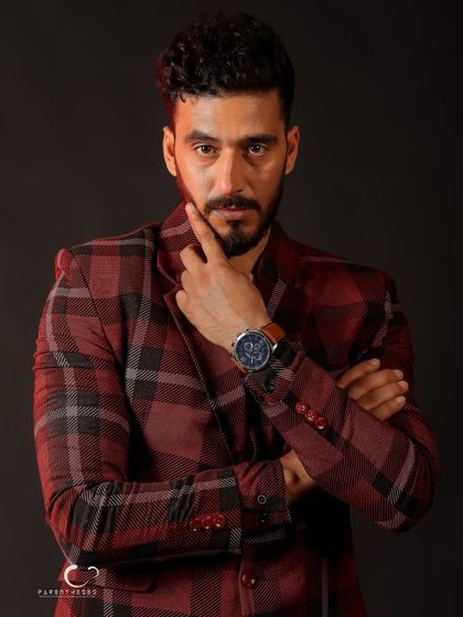 A classic headshot with a thoughtful expression. The plaid suit adds texture and character, while the lighting creates a moody and sophisticated feel.